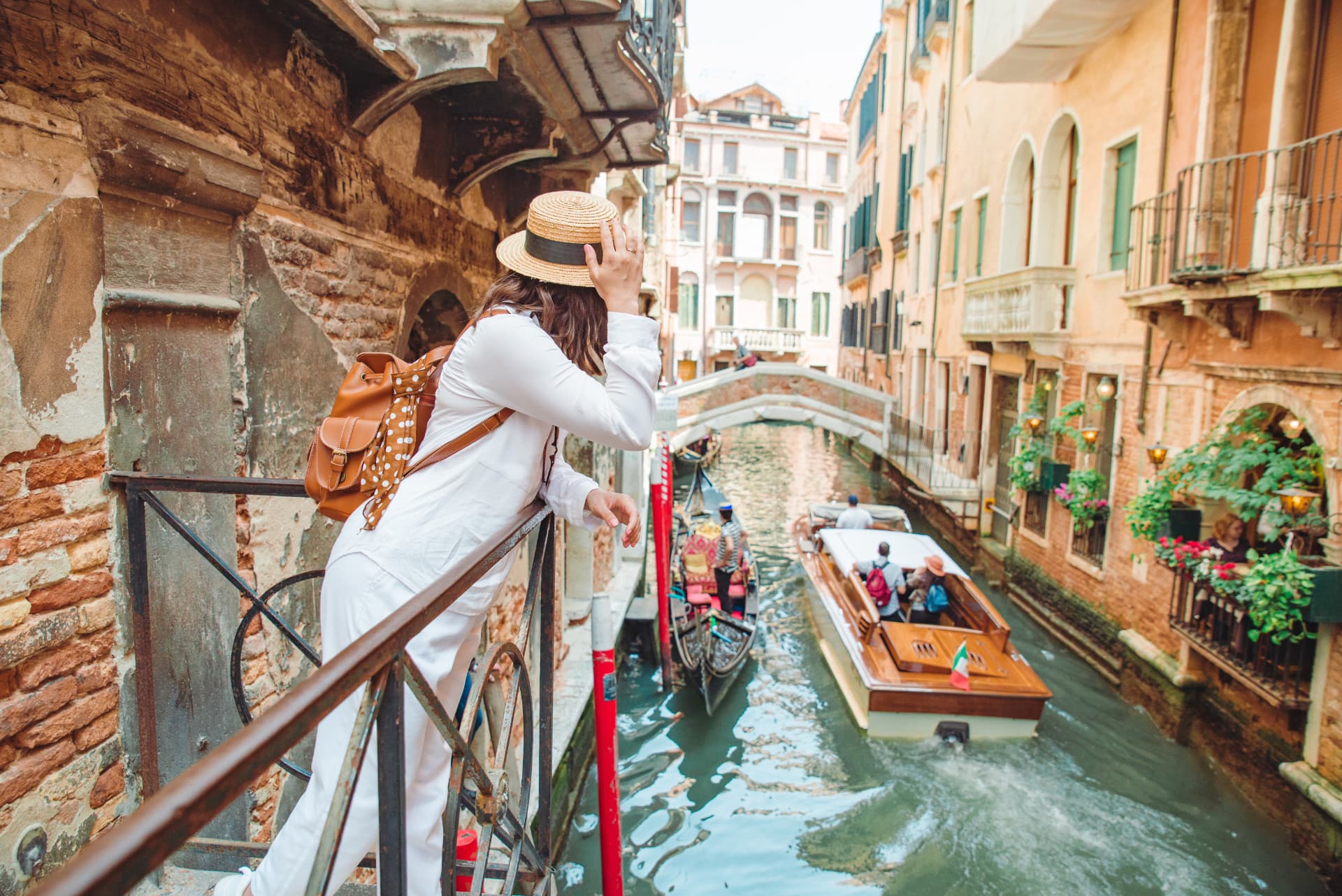 Traveler with a straw hat looking over a canal in Venice