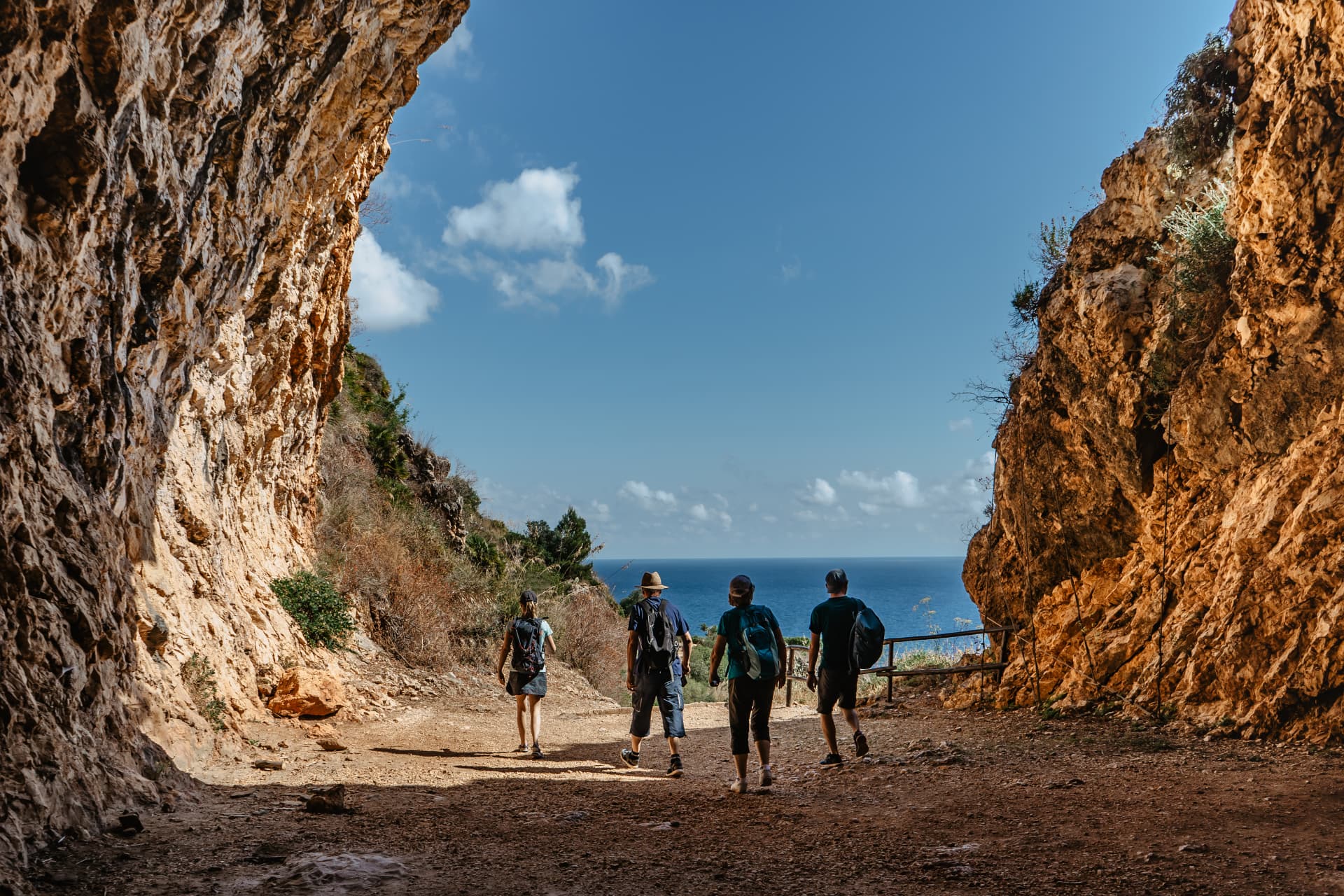 A small group of travellers walking along a coastal path framed by rocky cliffs